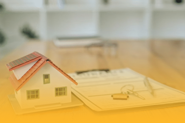 Model house placed on documents and blueprints on a desk, representing home buying and real estate planning.